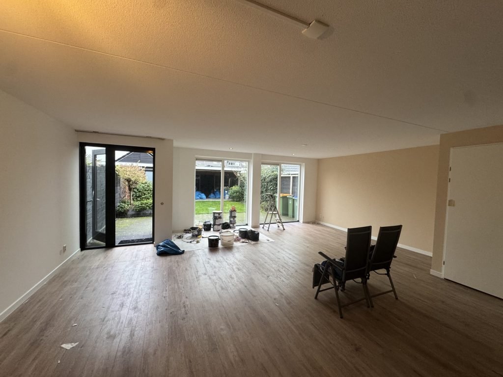 Lege woonkamer met houten vloer, tuindeuren en verfemmers klaar voor de afwerking